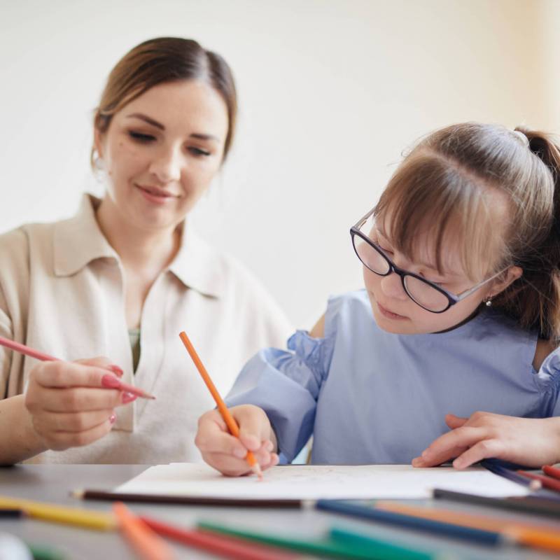 Portrait of cute teenage girl with down syndrome doing homework with caring mother helping her